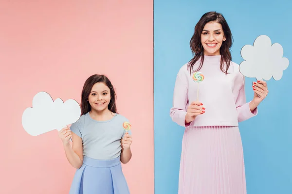 Adorable niño y atractiva mujer sosteniendo el habla burbujas y caramelos sobre fondo azul y rosa - foto de stock