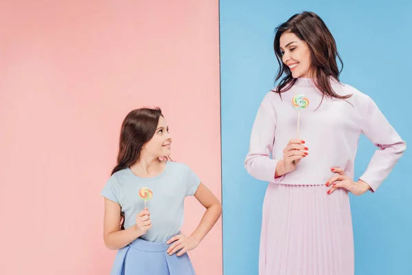 Очаровательный ребенок и привлекательная женщина улыбаясь и держа леденцы на голубом и розовом фоне — стоковое фото