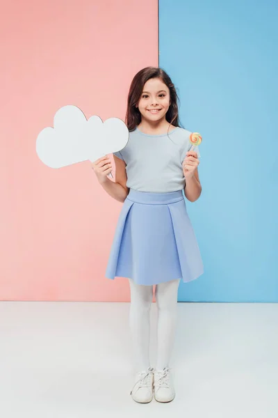 Очаровательный ребенок держит конфеты и речи пузырь, глядя на камеру на синем и розовом фоне — стоковое фото