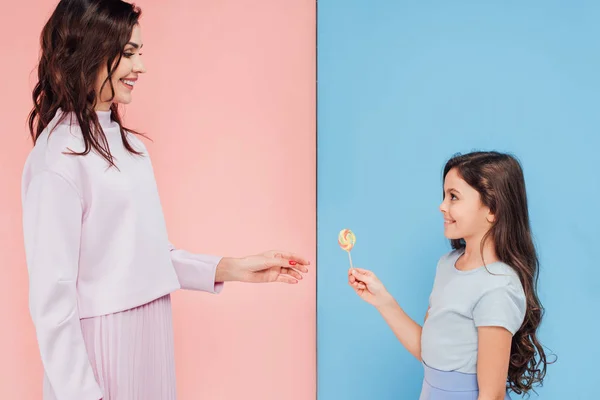 Adorable child giving candy to woman on blue and pink background — Stock Photo