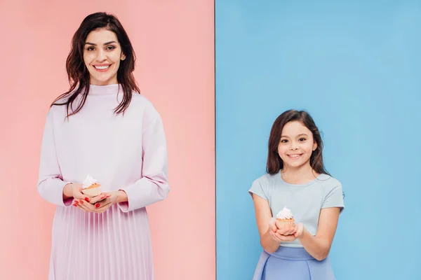 Hermosa mujer y niño sosteniendo cupcakes y mirando a la cámara sobre fondo azul y rosa - foto de stock