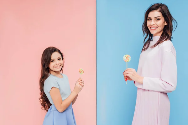 Красивая женщина и ребенок держат конфеты, глядя на камеру на синем и розовом фоне — стоковое фото