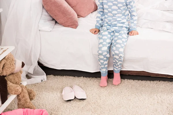 Cropped view of kid in pajamas sitting on bed in bedroom — Stock Photo