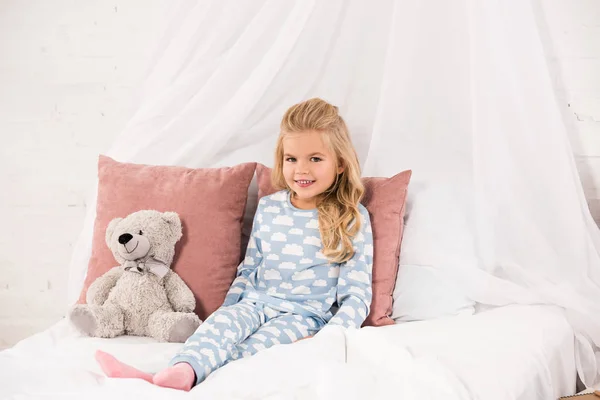Adorable enfant assis sur le lit avec ours en peluche — Photo de stock