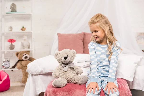 Lächelndes süßes Kind sitzt mit Teddybär im Bett — Stockfoto