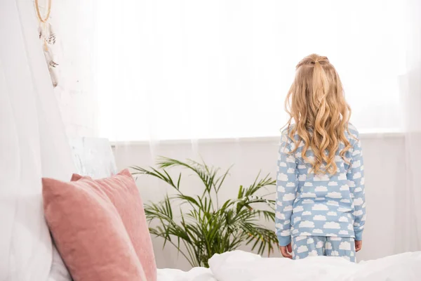 Вид сзади ребенка в пижаме, стоящего у окна в спальне — стоковое фото