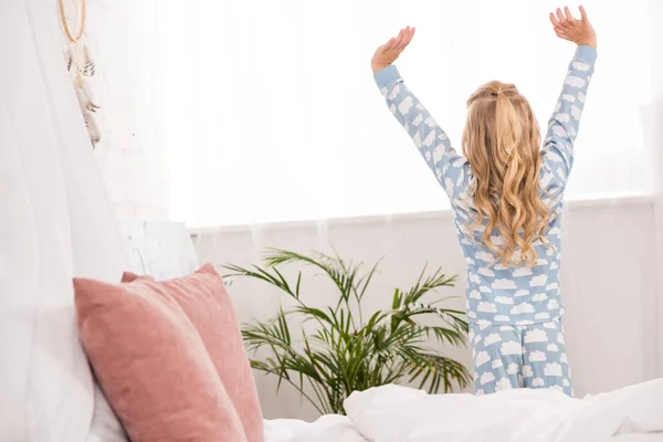 Vista trasera del niño en pijama que se extiende cerca de la ventana en el dormitorio - foto de stock