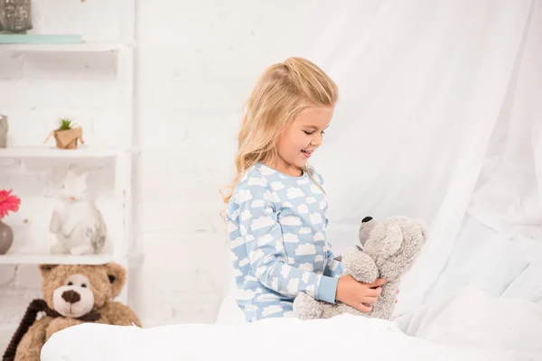 Весела дитина грає з плюшевим ведмедем у ліжку — стокове фото