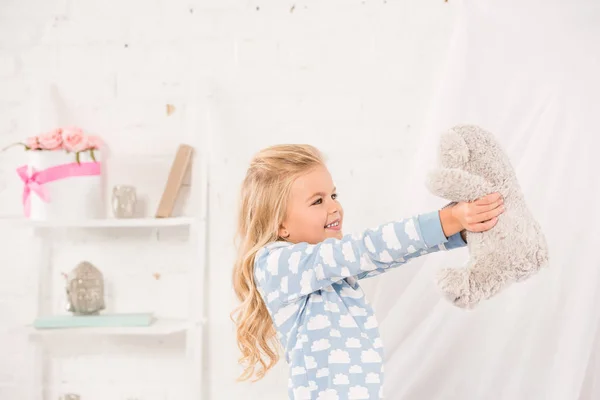 Sonriente lindo niño jugando con osito de peluche en dormitorio - foto de stock