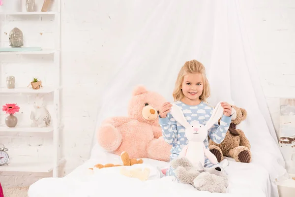 Sonriente lindo niño jugando con suave juguetes en la cama - foto de stock