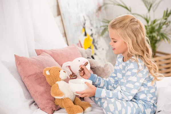 Adorable child in pajamas feeding soft toys in bed — Stock Photo