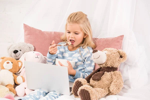 Cute child eating cornflakes and watching cartoons in bed — Stock Photo