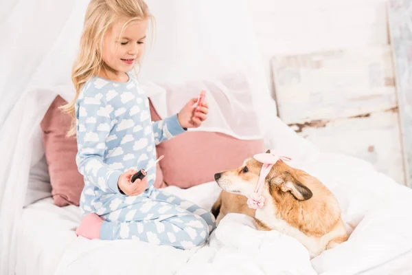 Lindo niño con brillo de labios mirando perro corgi con accesorios rosados - foto de stock