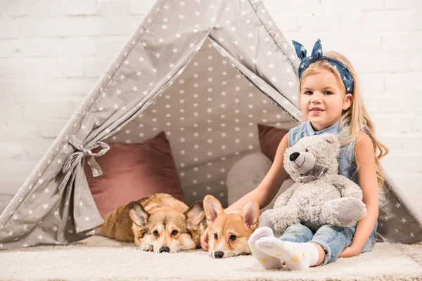 Adorable enfant avec des chiens corgi gallois et ours en peluche à wigwam à la maison — Photo de stock