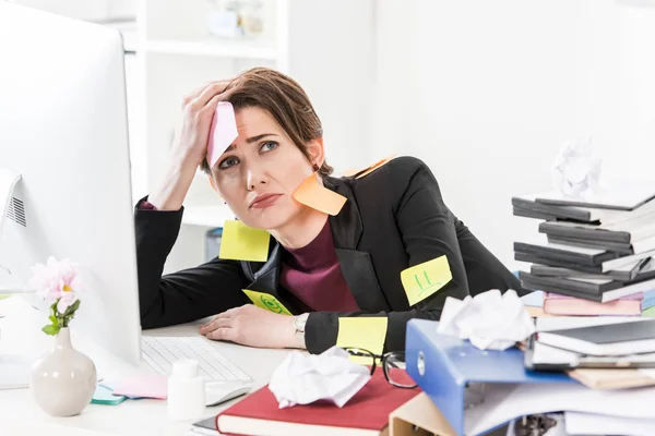 Грустная привлекательная деловая женщина сидит с наклейками на лице и одежде в офисе — стоковое фото
