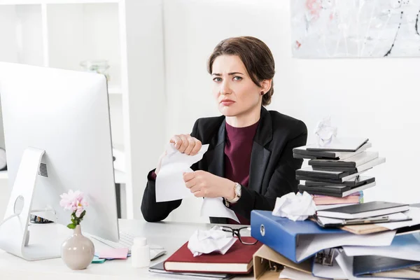 Sad attractive businesswoman tearing documents in office — Stock Photo