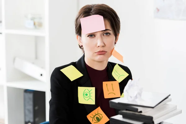 Depressed attractive businesswoman sitting with stickers on face and clothes in office — Stock Photo