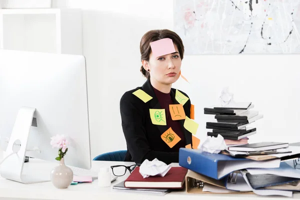 Upset attractive businesswoman sitting with stickers on face and clothes in office, looking at camera — Stock Photo