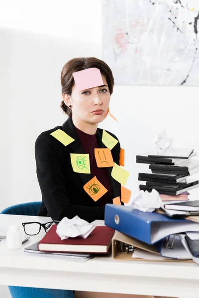Sad attractive businesswoman sitting with stickers on face and clothes in office — Stock Photo