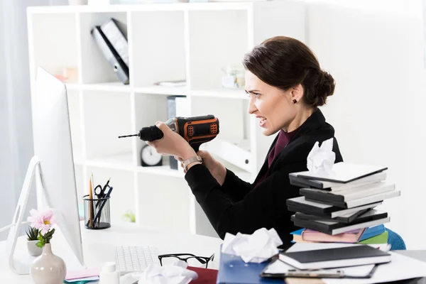 Vista lateral da mulher de negócios atraente irritado segurando broca elétrica no escritório — Fotografia de Stock