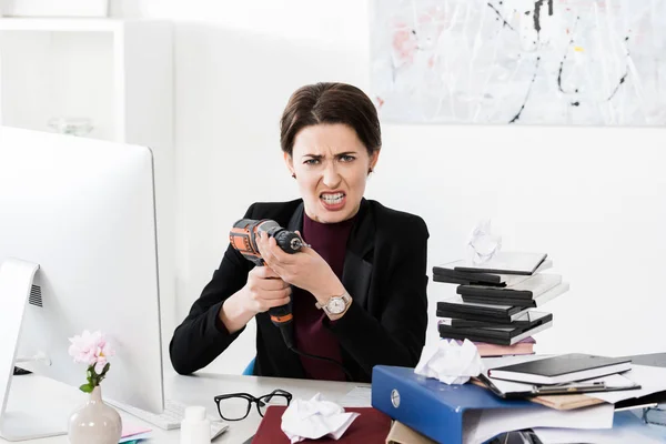 Агресивний привабливий бізнес-леді проведення Електродрилі в офіс і дивлячись на камеру — стокове фото