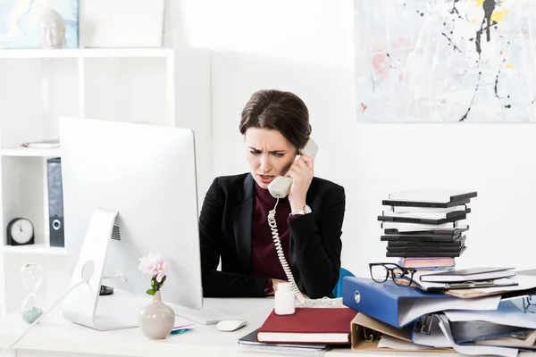 Сердитая привлекательная деловая женщина разговаривает по стационарному телефону в офисе — стоковое фото