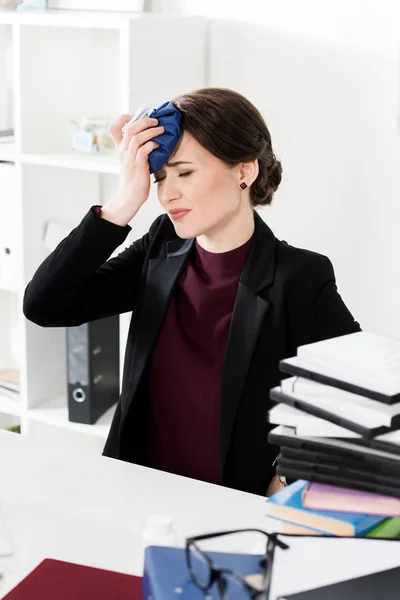 Unhealthy businesswoman touching head with ice pack in office — Stock Photo
