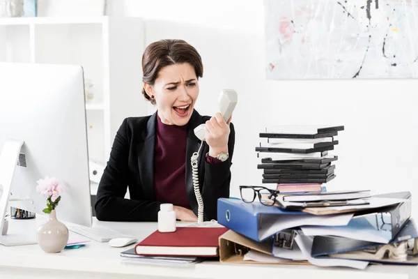 Femme d'affaires attrayante en colère criant tout en parlant par téléphone fixe dans le bureau — Photo de stock