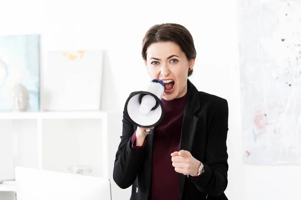 Angry businesswoman screaming in megaphone in office, looking at camera — Stock Photo