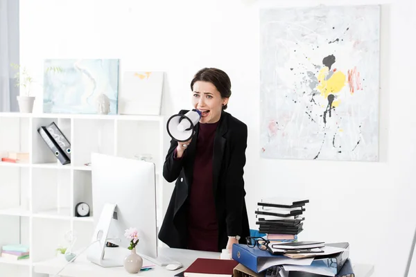 Angry businesswoman screaming in megaphone in office, looking away — Stock Photo