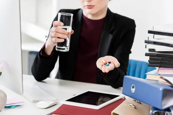 Обрезанный образ предпринимательницы, держащей стакан воды и таблетки в офисе — стоковое фото