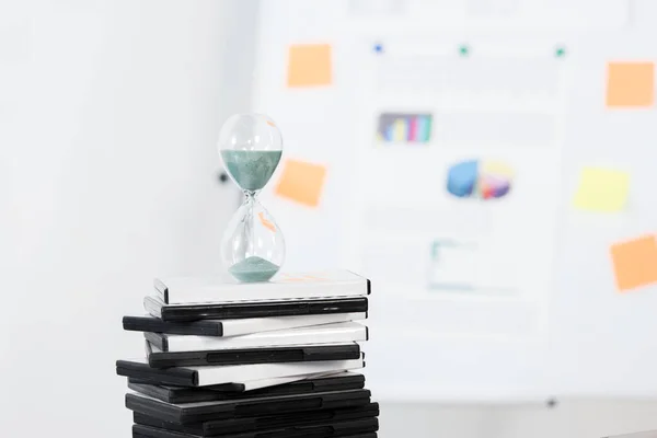Hourglass on stack of DVDs in light business office — Stock Photo