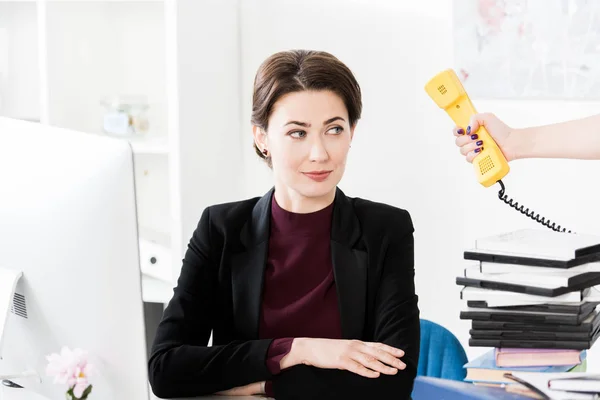 Secretário dando telefone amarelo estacionário para bela empresária no escritório — Fotografia de Stock