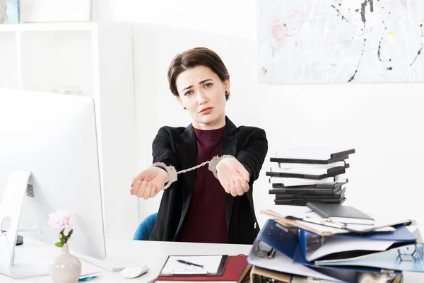 Traurige Geschäftsfrau zeigt Hände mit Handschellen am Tisch im Büro — Stockfoto