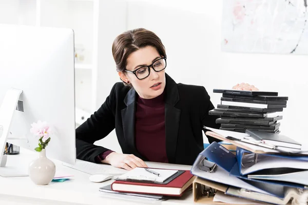 Приваблива бізнес-леді в окулярах дивиться на стос документів в офісі — стокове фото
