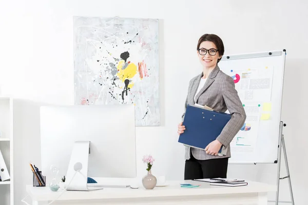 Attraktive Geschäftsfrau hält Ordner mit Dokumenten im Büro und blickt in die Kamera — Stockfoto