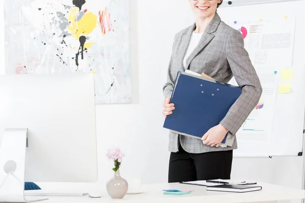 Immagine ritagliata di donna d'affari sorridente che tiene la cartella con documenti in ufficio — Foto stock