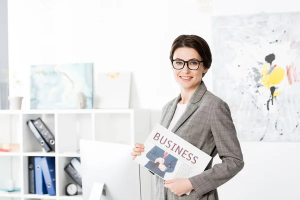 Привлекательная деловая женщина держит газету в офисе и смотрит в камеру — стоковое фото