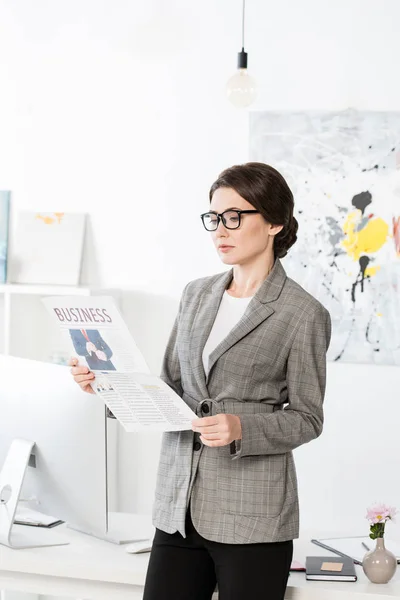 Attractive businesswoman reading business newspaper in office — Stock Photo
