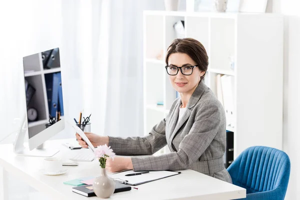 Attraktive Geschäftsfrau mit Zeitung im Büro und Blick in die Kamera — Stockfoto