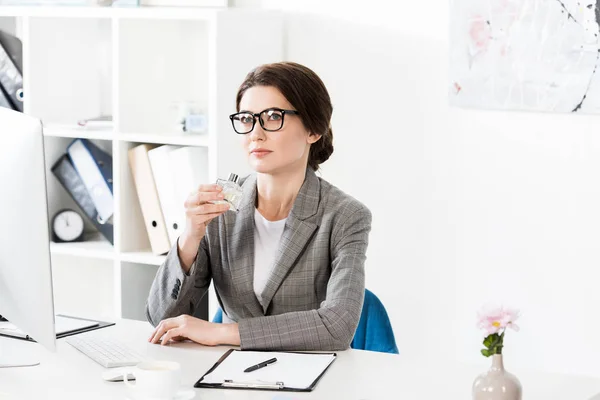 Attractive businesswoman sniffing jar of perfume in office — Stock Photo