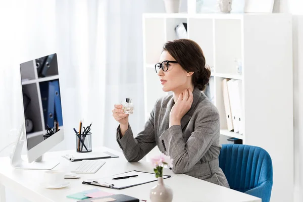 Attrayant femme d'affaires appliquant du parfum sur le cou dans le bureau — Photo de stock