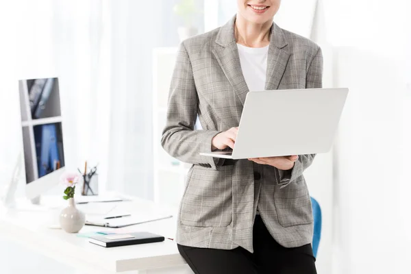 Обрезанный образ улыбающейся бизнесвумен с помощью ноутбука в офисе — стоковое фото