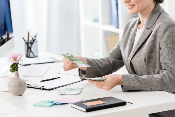 Imagen recortada de la mujer de negocios contando billetes en euros en la mesa en el cargo - foto de stock