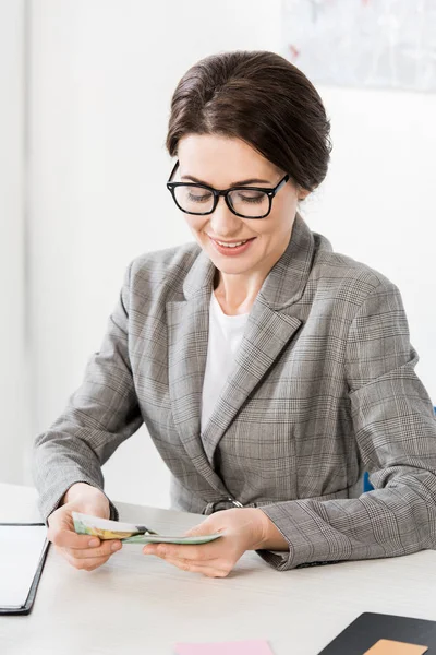 Attractive businesswoman looking at euro banknotes in office — Stock Photo
