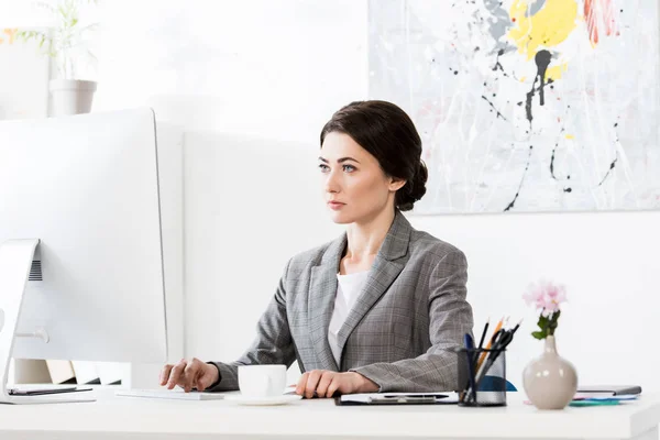 Ernsthafte attraktive Geschäftsfrau im grauen Anzug sitzt mit Computer im Büro — Stockfoto
