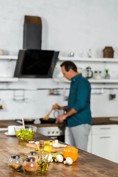 Selective focus of mature man frying vegetables in kitchen, spices on tabletop — Stock Photo