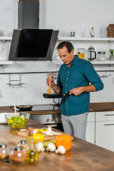 Messa a fuoco selettiva di bello uomo maturo che cucina verdure in cucina — Foto stock