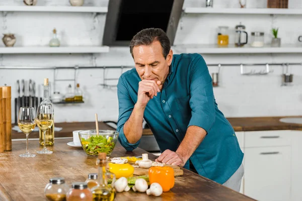 Schöner reifer Mann lehnt sich auf den Tisch und betrachtet Gemüse in der Küche — Stockfoto