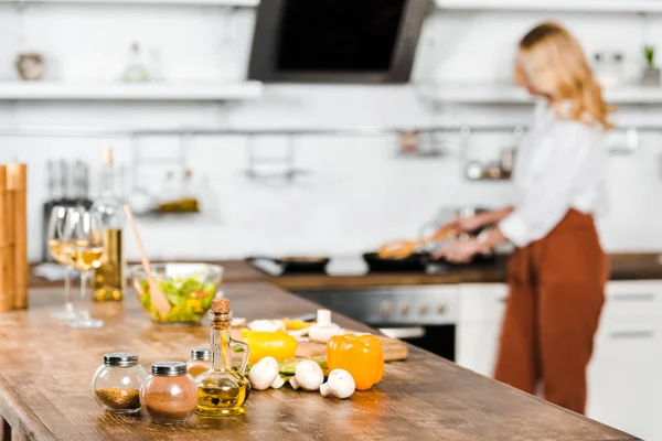 Enfoque selectivo de la mujer madura cocinar verduras en la sartén en la cocina, especias en la mesa - foto de stock